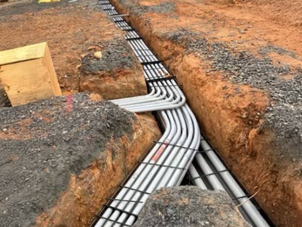 Electrical conduits bending through an excavated underground trench with spacers installed