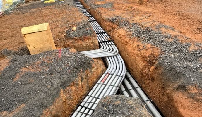 Electrical conduits bending through an excavated underground trench with spacers installed