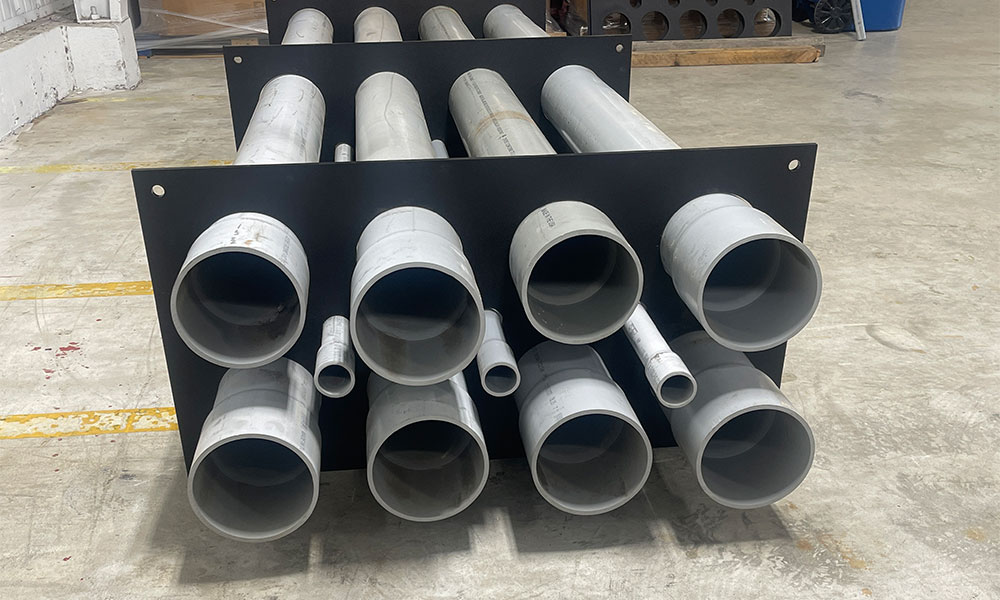 Black metal rack holding assorted gray PVC pipes on a concrete warehouse floor.